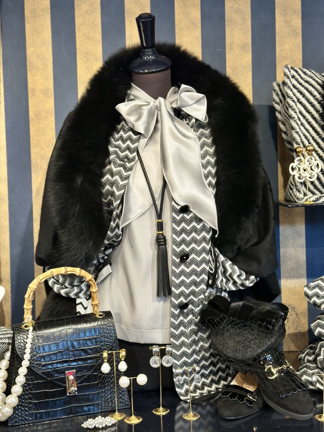 Elegant damesoutfit met zwart-witte print, zijden strik en accessoires, perfect voor modieuze gelegenheden.foresti vest zwart wit Missoni motief