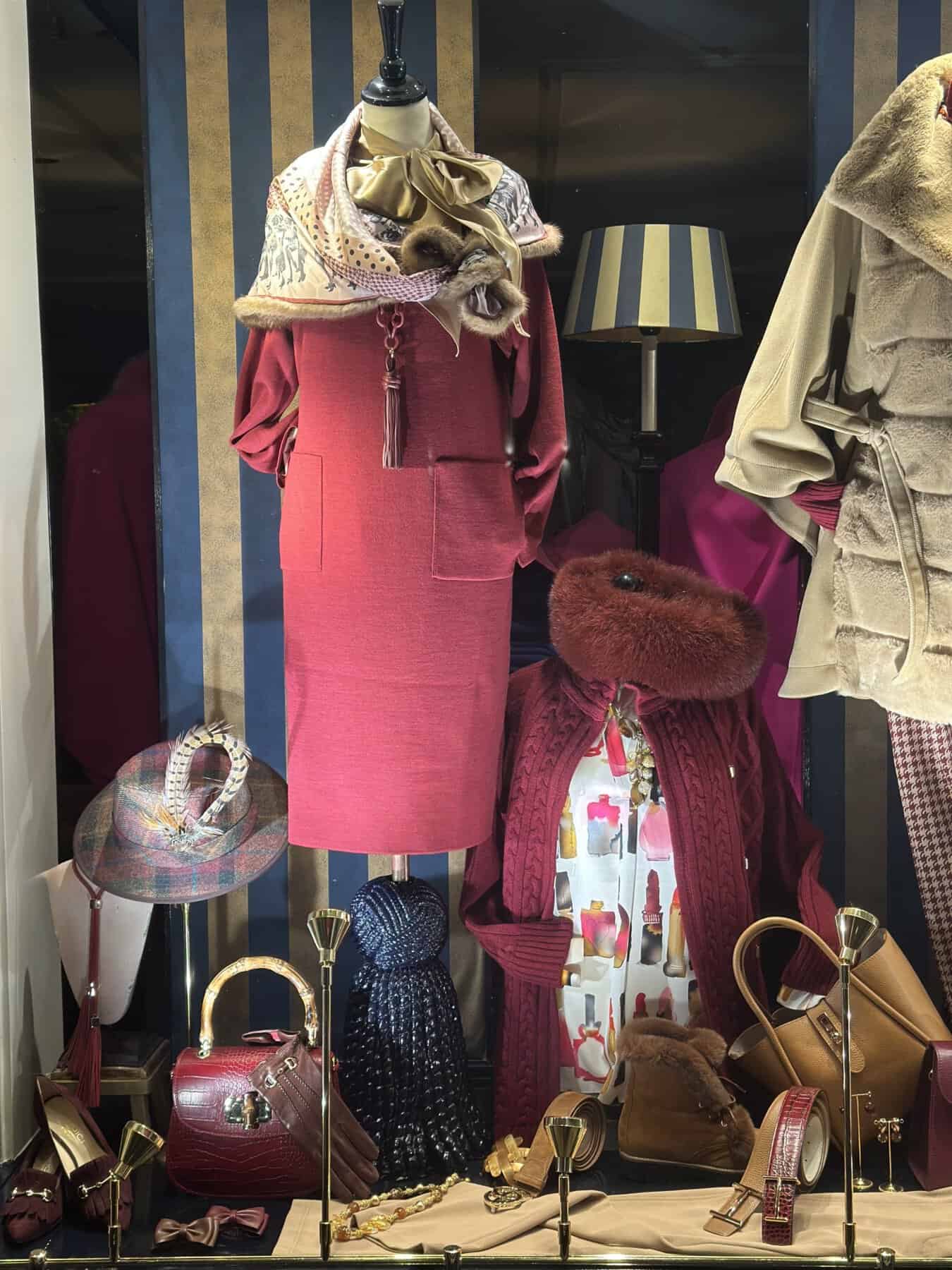 Elegant vintage damesoutfit met roze jurk en stijlvolle accessoires in een winkelraam.